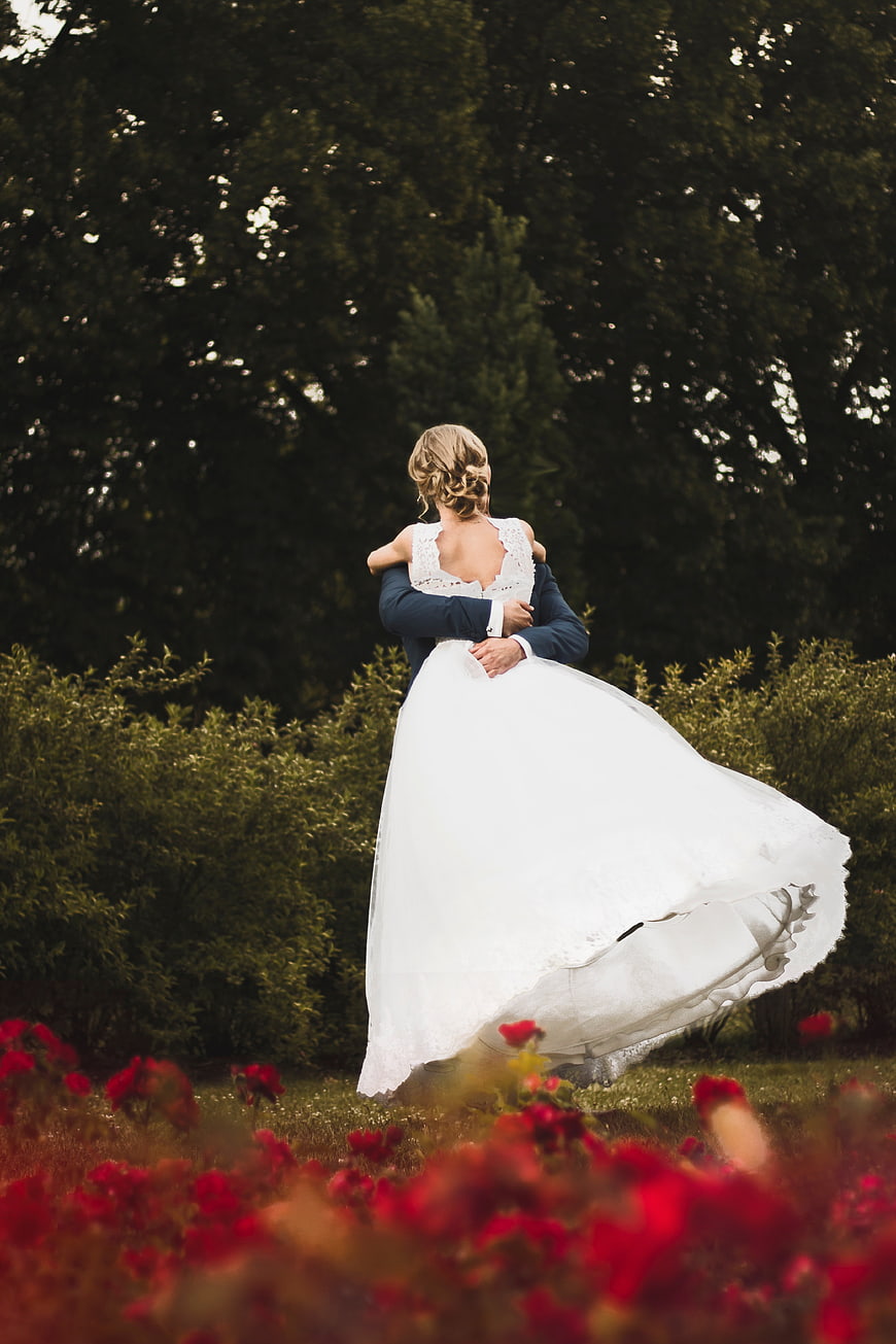 Romantic Wedding Couple Embracing in Garden with Red Flowers