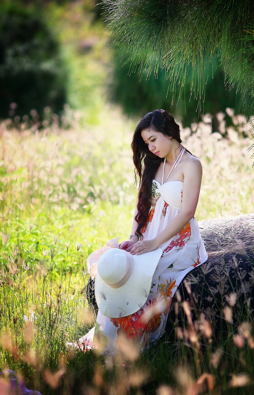 Woman in Floral Dress Sitting in Grassy Field with Hat