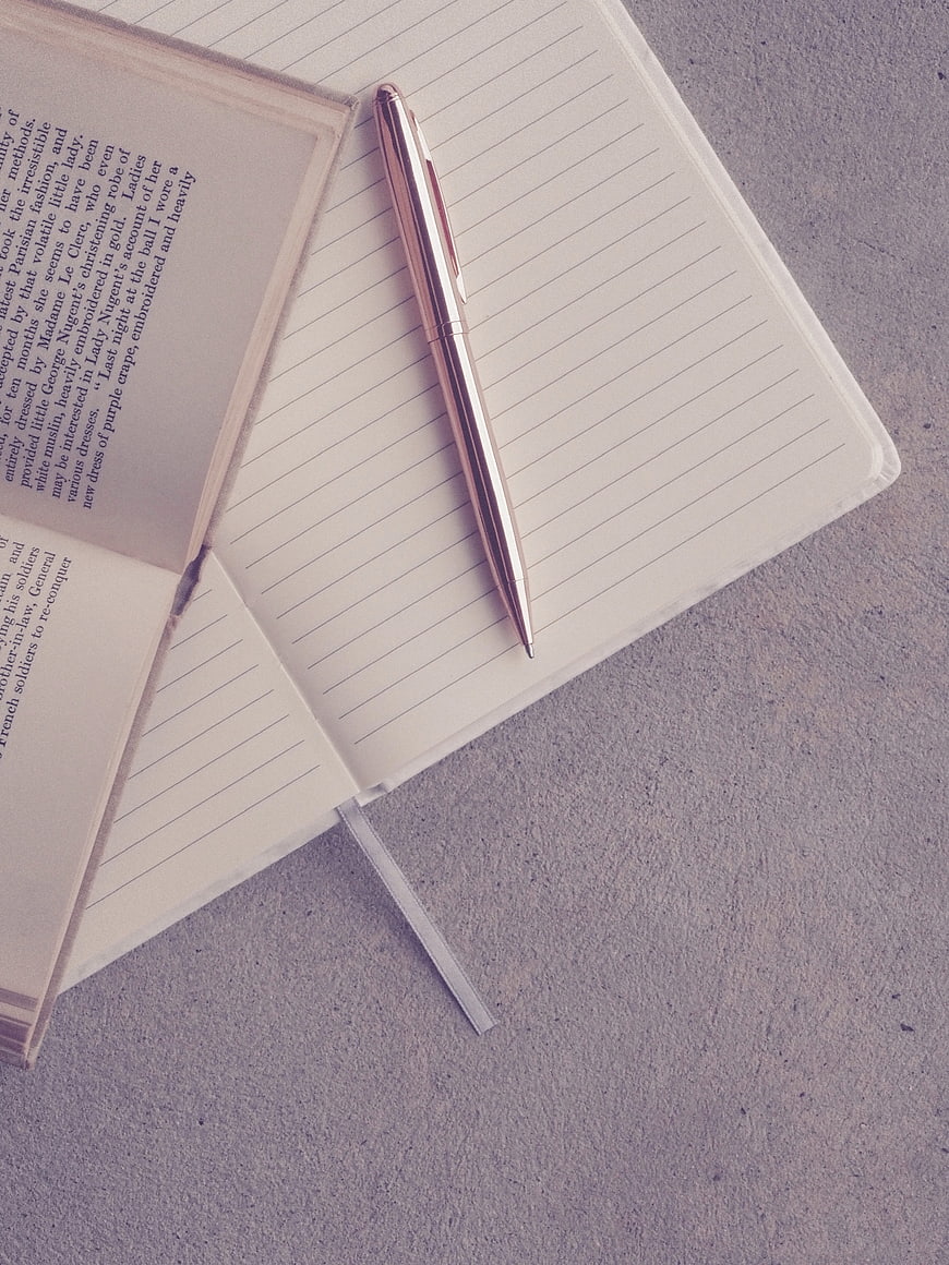 Open Notebook and Rose Gold Pen on Gray Concrete Surface