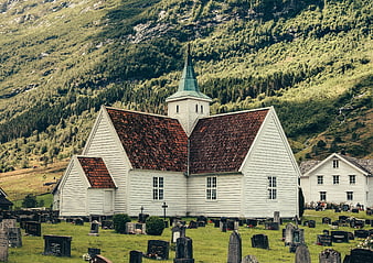 White wooden church with cemetery in green mountain valley