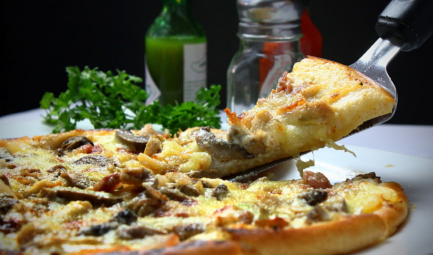 Close-up of cheesy mushroom pizza slice being lifted