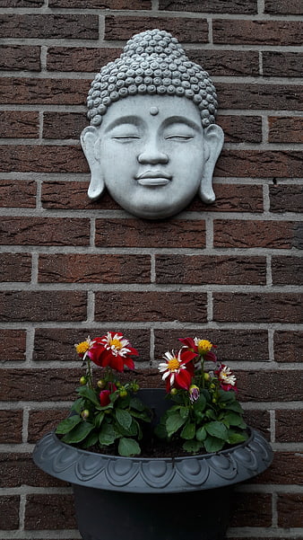 Serene Buddha Head Sculpture on Brick Wall with Flowers
