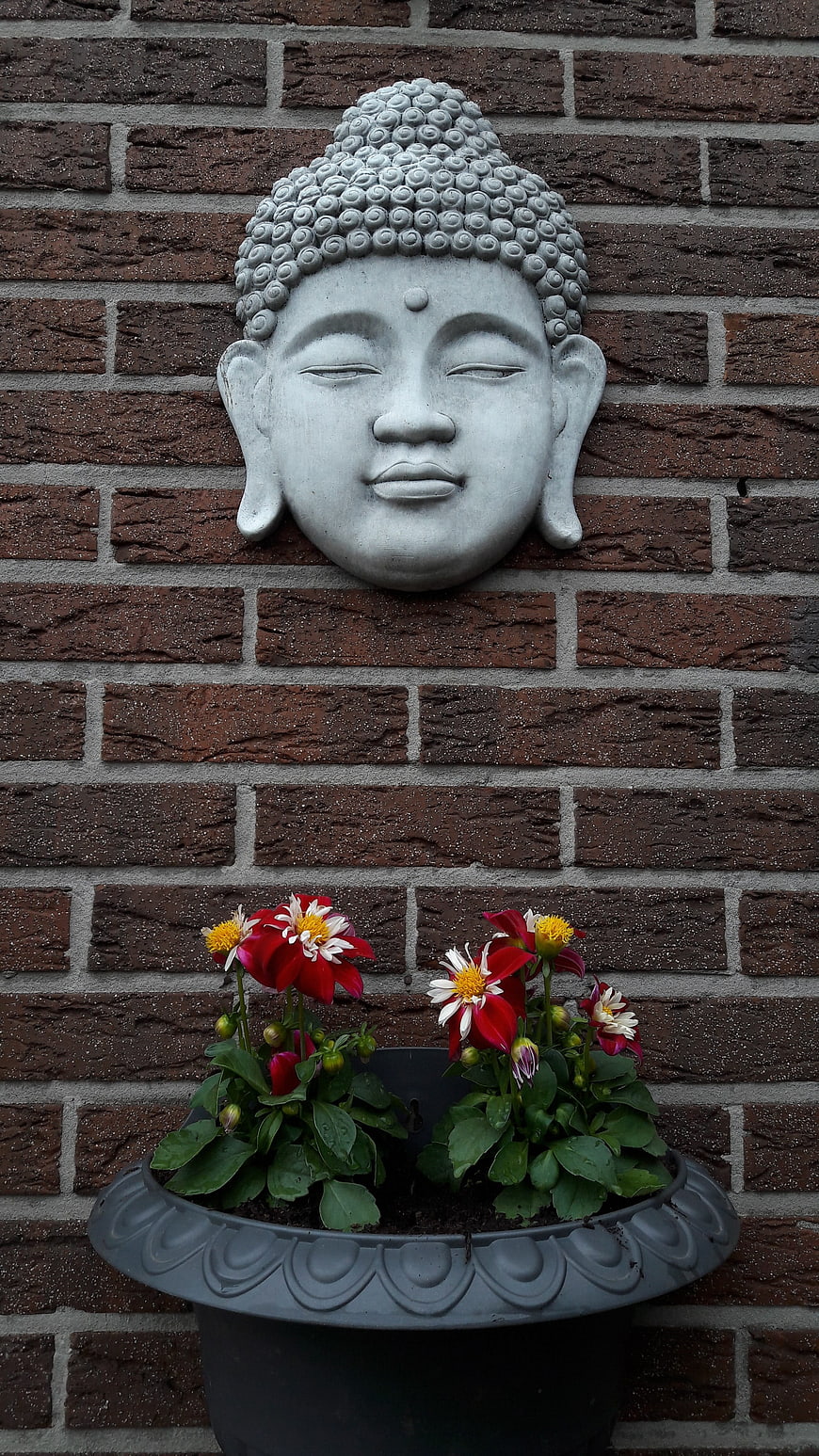 Serene Buddha Head Sculpture on Brick Wall with Flowers