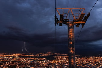 Lightning Storm Over City Lights at Night with Cable Car Tower