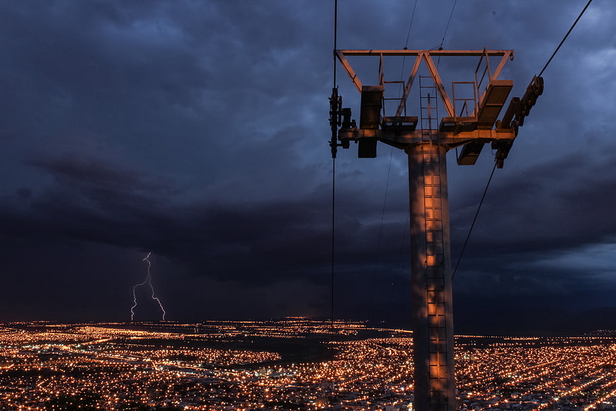 Lightning Storm Over City Lights at Night with Cable Car Tower