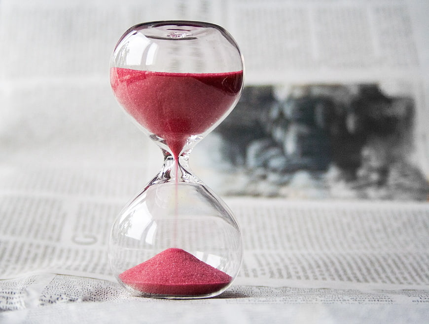 Red Sand Hourglass on Newspaper Background
