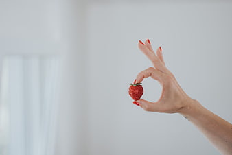 Woman's Hand Holding Fresh Strawberry with Red Nails