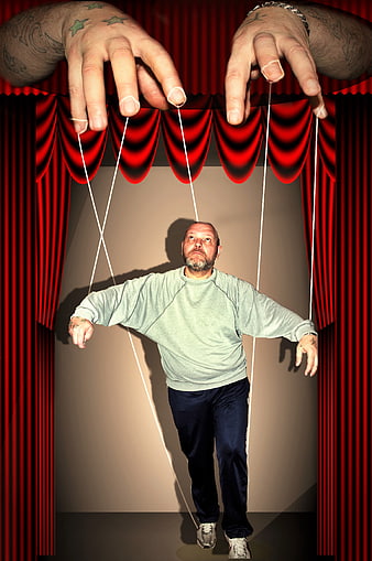 Conceptual man as puppet on stage with red curtains and control strings