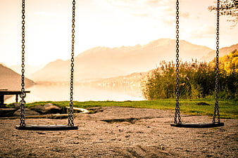 Empty swings overlooking a lake and mountains at sunset