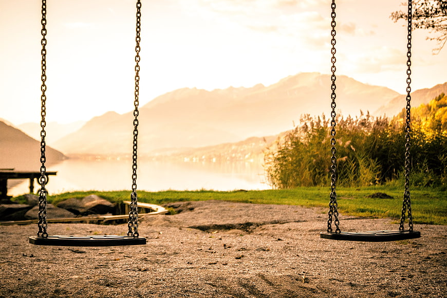 Empty swings overlooking a lake and mountains at sunset