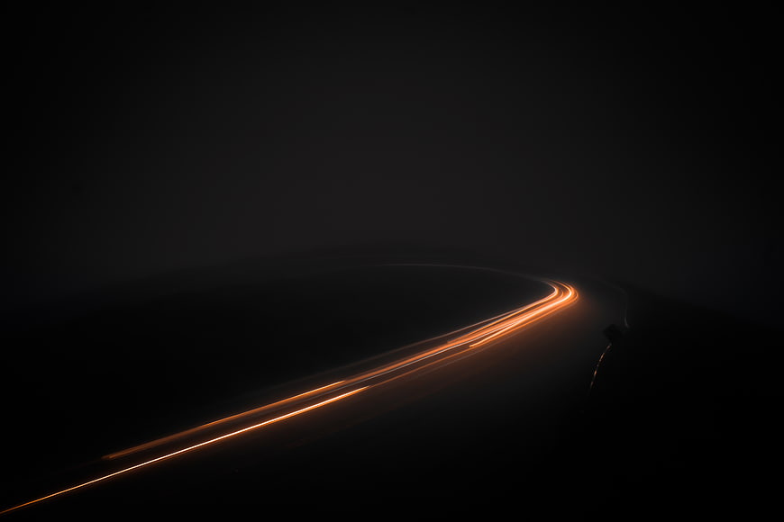 Orange light trails on a dark winding road at night