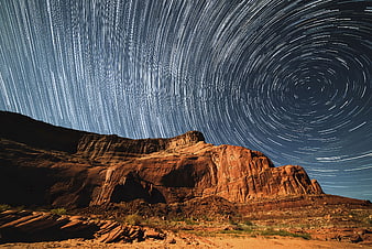 Star trails circling Polaris over red desert rock formations