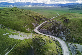 Aerial view of winding road through green rolling hills and mountains