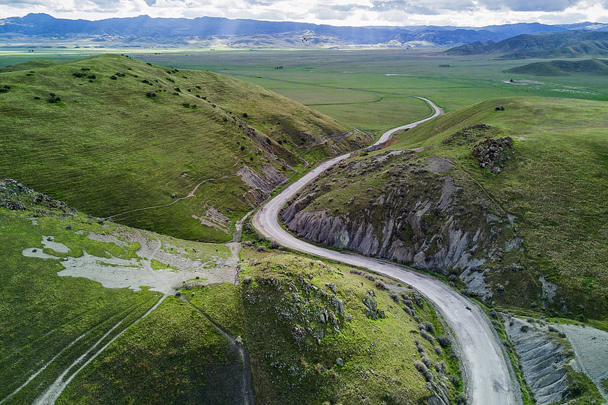 Aerial view of winding road through green rolling hills and mountains