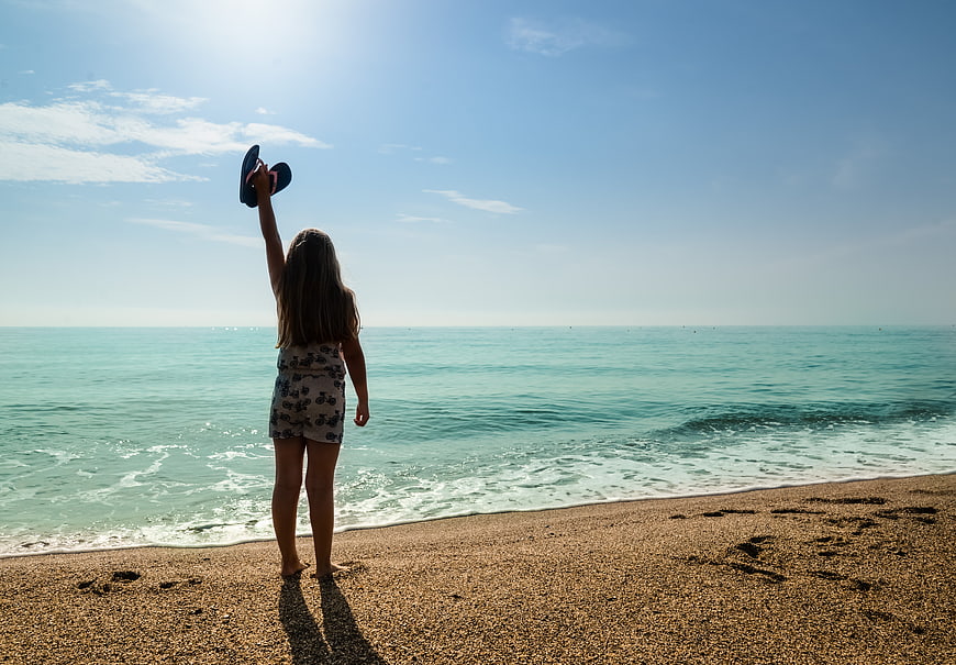 Girl holding flip flops on sunny beach