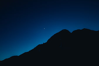 Silhouette of mountain ridge against deep blue twilight sky with crescent moon