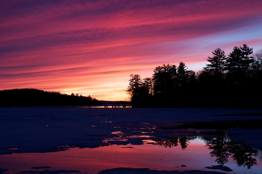 Vibrant pink and purple sunset over frozen lake with tree silhouettes