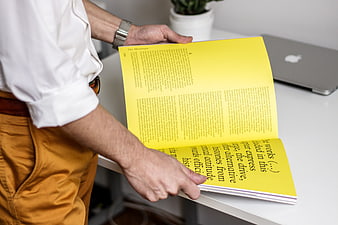 Man holding yellow magazine at white desk