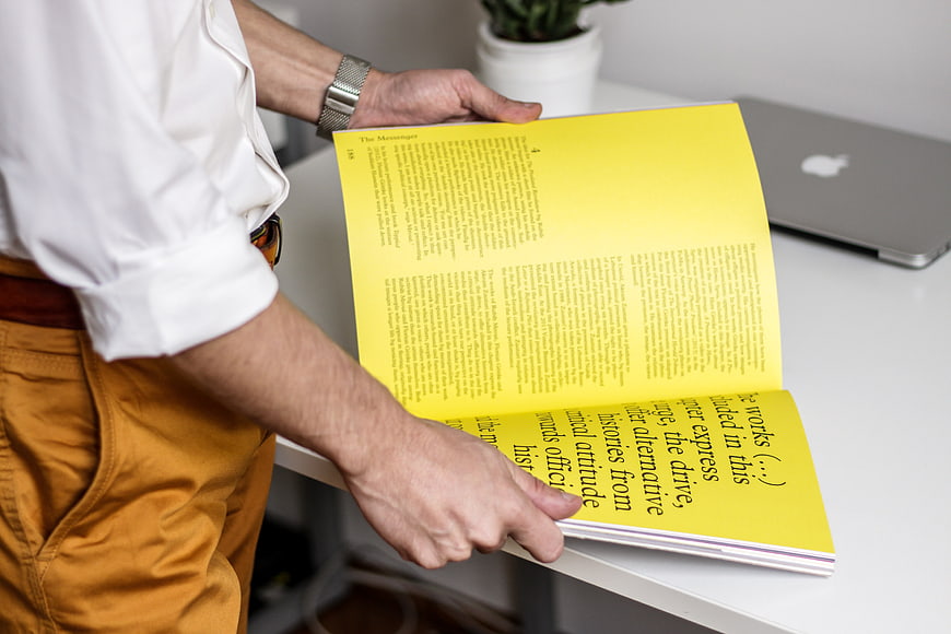 Man holding yellow magazine at white desk
