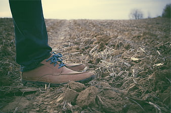 Man's brown shoes standing on plowed agricultural field soil