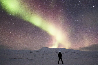 Silhouette of person watching aurora borealis over snowy mountain landscape at night