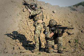 Two soldiers in tactical gear aiming rifles in desert terrain