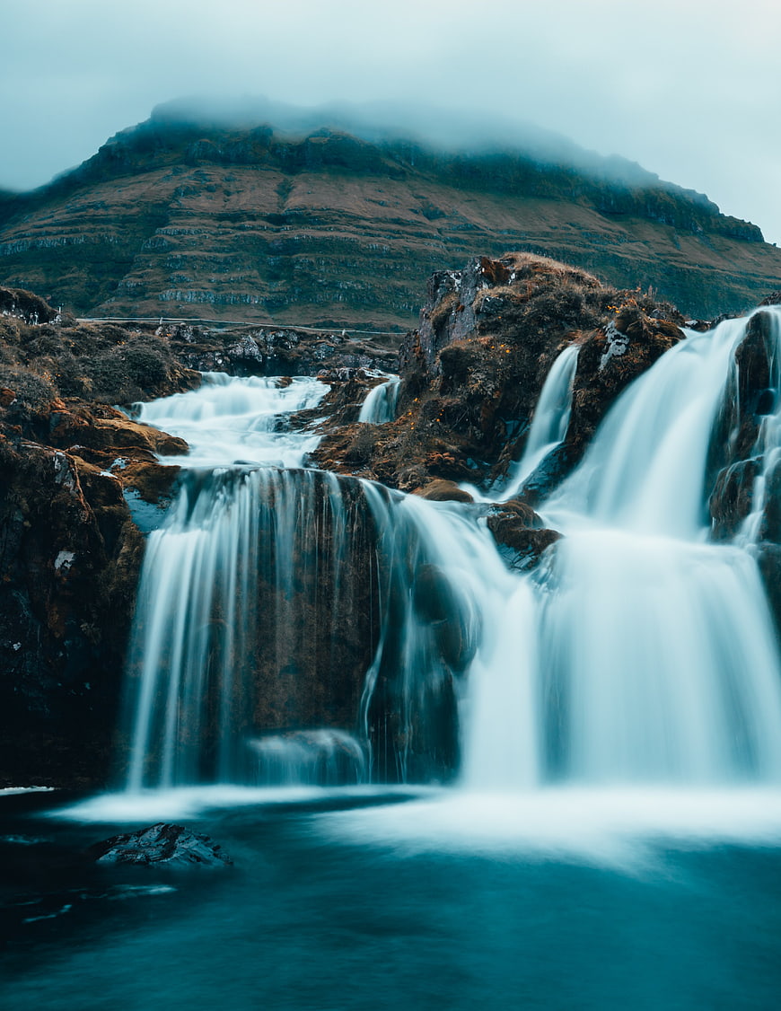Misty waterfall cascading over rocks with mountain backdrop