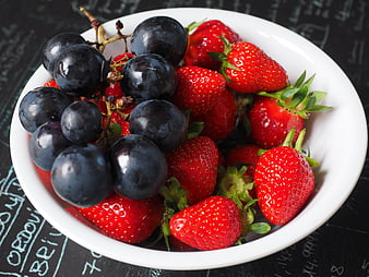 Fresh strawberries and black grapes in a white bowl