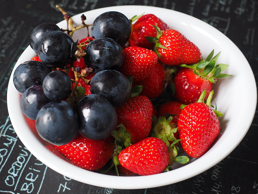 Fresh strawberries and black grapes in a white bowl