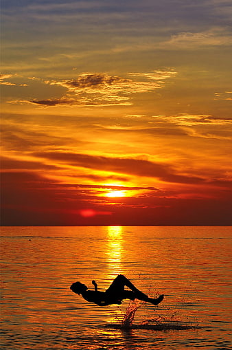 Silhouette of Person Jumping into Ocean at Sunset