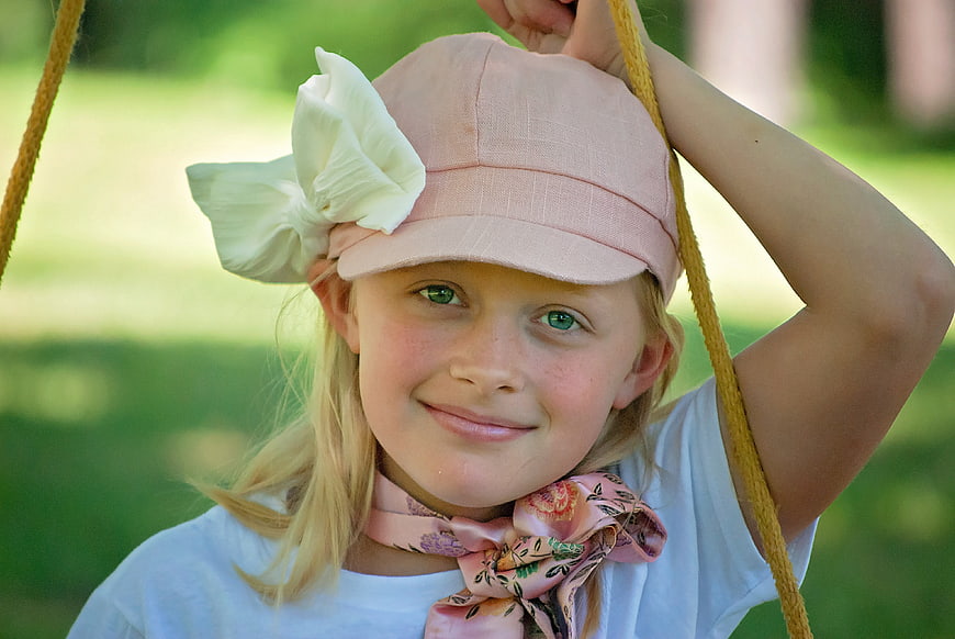 Smiling young girl in pink hat and scarf on a swing