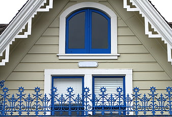 Beige house facade with blue windows and ornate metal fence