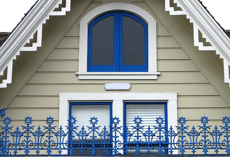 Beige house facade with blue windows and ornate metal fence