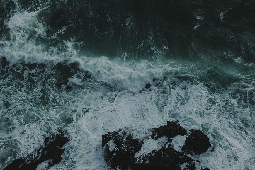Aerial view of crashing ocean waves on dark rocks