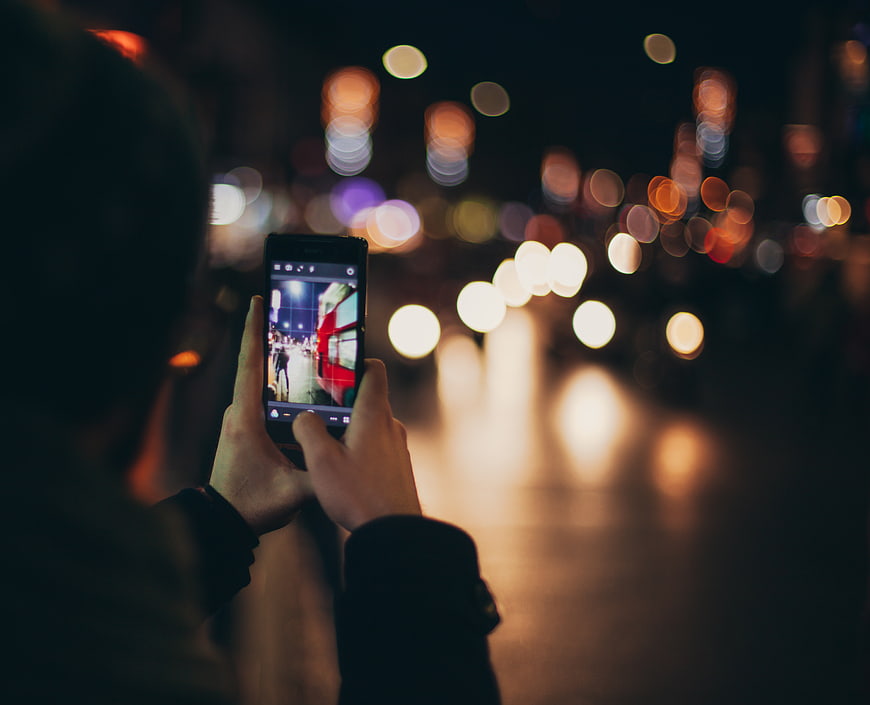 Person taking photo of city street at night with smartphone