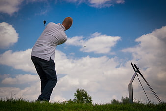 Golfer Swinging Club on Green Grass Under Blue Sky