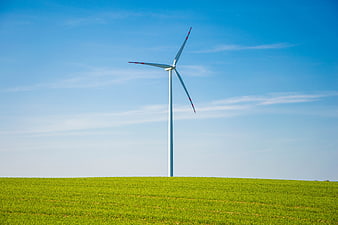 Single wind turbine standing in a green field under a blue sky