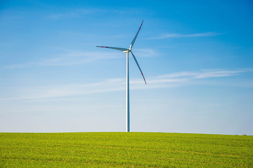 Single wind turbine standing in a green field under a blue sky