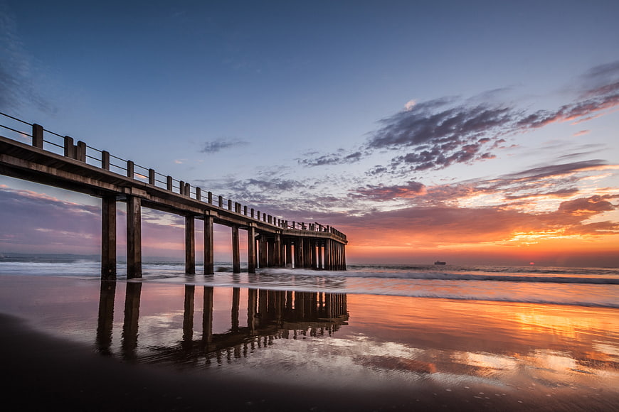 Sunrise Over Wooden Pier With Reflections On Wet Sand