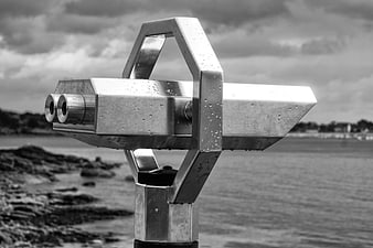 Wet metal telescope on rocky coast with cloudy sky