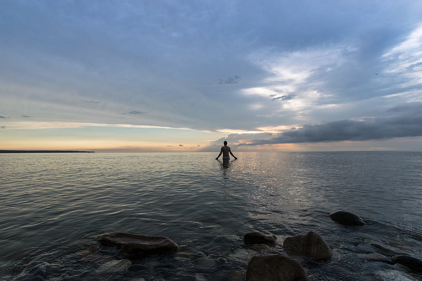 Man Standing in Ocean Water at Sunset with Rocky Shore