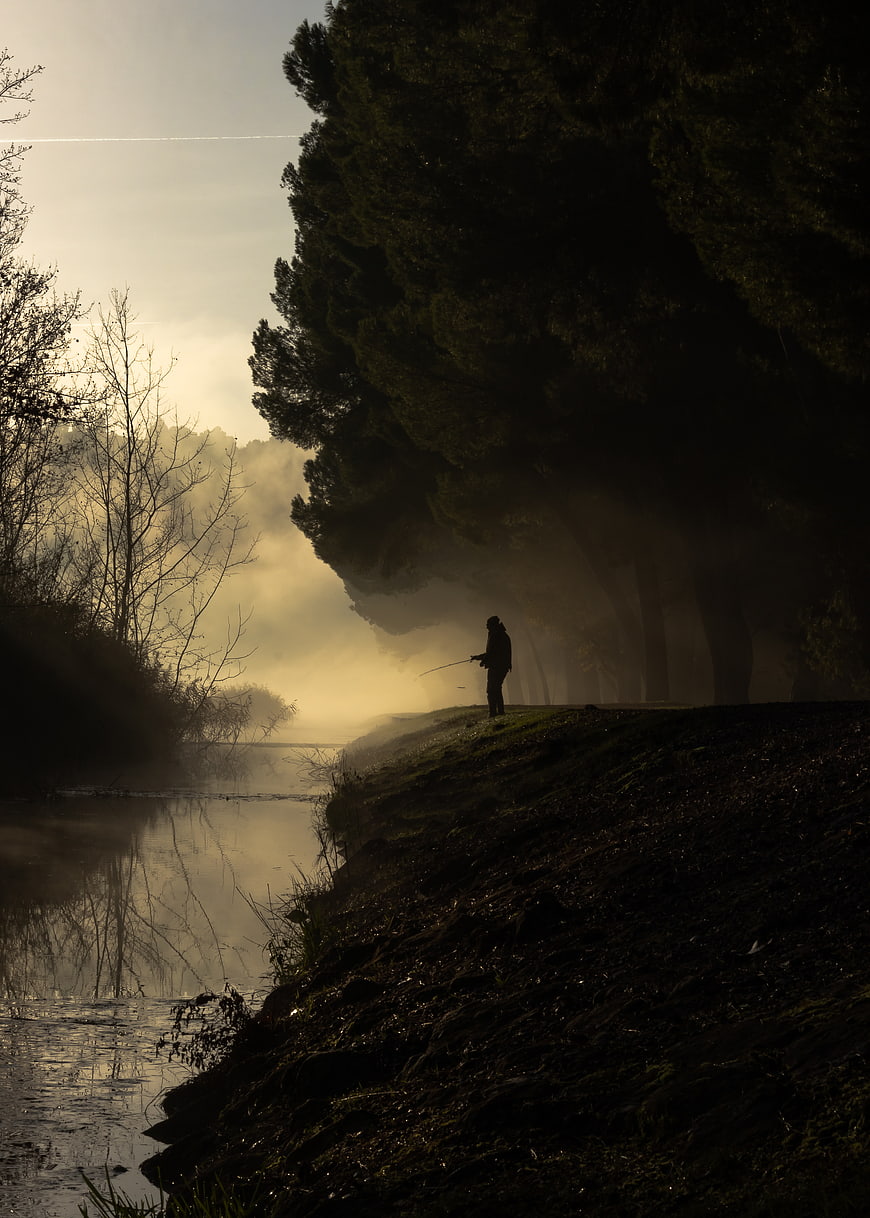 Silhouette of fisherman on misty riverbank at dawn