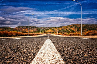 Empty asphalt road with white center line leading to distant hills