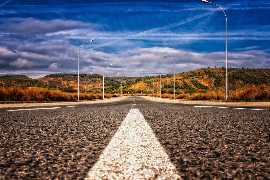 Empty asphalt road with white center line leading to distant hills