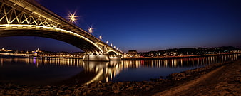 Illuminated steel arch bridge over river at night with city skyline