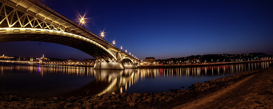 Illuminated steel arch bridge over river at night with city skyline