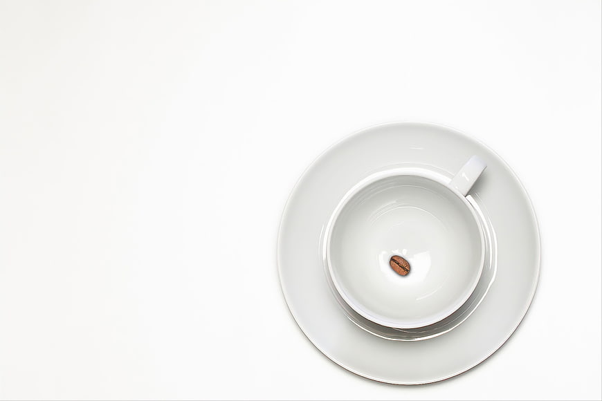 Empty white coffee cup with single bean on saucer, top view