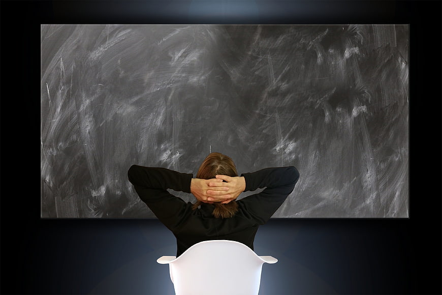Woman sitting in front of empty chalkboard thinking
