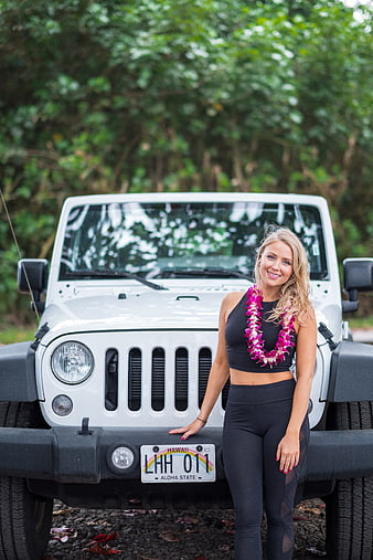 Blonde woman with lei posing by white Jeep in Hawaii