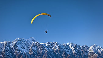 Paraglider flying over snow-capped mountains against blue sky